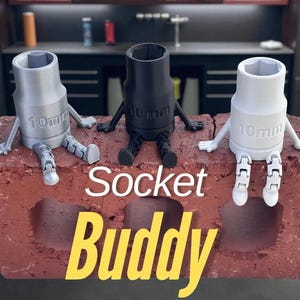 Puede incluir: Tres llaves de vaso en plata, negro y blanco, cada una con brazos y piernas, sentadas sobre un ladrillo rojo. Las llaves están etiquetadas como "10mm" y el texto "Socket Buddy" se muestra en amarillo.