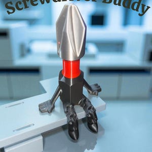 May include: A novelty screwdriver bit with a silver head, red collar, and black body, arms, and legs. The text "Screwdriver Buddy" is arched above the figure. The figure is sitting on a light gray surface.