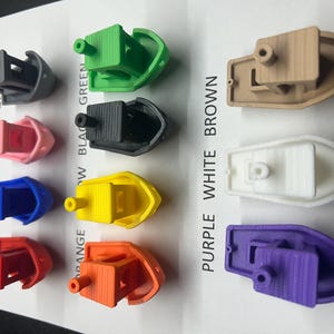 K&ouml;nnte beinhalten: Eine Sammlung kleiner, farbiger Boote in verschiedenen Farben, darunter Grau, Gr&uuml;n, Rosa, Schwarz, Blau, Gelb, Rot, Orange, Braun, Wei&szlig; und Lila. Die Boote haben eine kleine Kabine und einen zylindrischen Vorsprung.