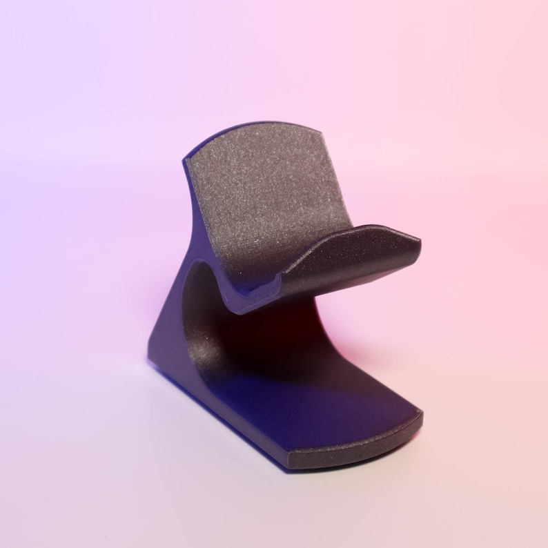 May include: A black stand with a curved design and a textured top. The stand has a rounded base and a curved support. The background fades from purple to pink.