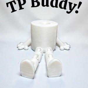 May include: A white 3D-printed toilet roll holder designed as a cartoon character. The holder has arms, legs, and the text "TP Buddy!" in black above it. The toilet roll is visible in the center.