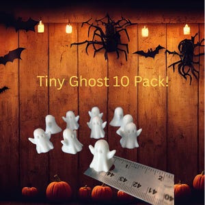 May include: A pack of ten small, white ghost figurines with outstretched arms, arranged on a wooden background. The text "Tiny Ghost 10 Pack!" is displayed. Halloween-themed decorations include pumpkins, bats, and spiders.