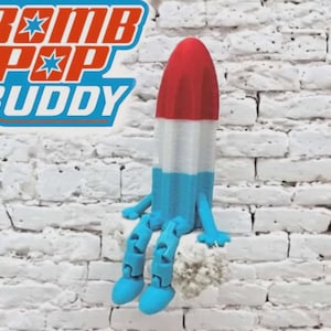 May include: A whimsical, colorful figurine resembling a popsicle, with red, white, and blue sections. The figurine has articulated blue legs and arms, and the text "BOMB POP BUDDY" is displayed in a stylized font.