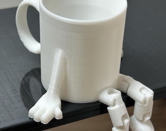 May include: A white ceramic mug with a curved handle and attached legs and feet, giving the appearance of a seated figure. The legs are articulated, allowing for posing. The mug is sitting on a dark surface.