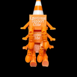 May include: An orange and white traffic cone figure with multiple articulated orange arms and legs. The central block features the text Emotional Support Cone printed in white. The figure has a pointed top and a square base with limbs attached.