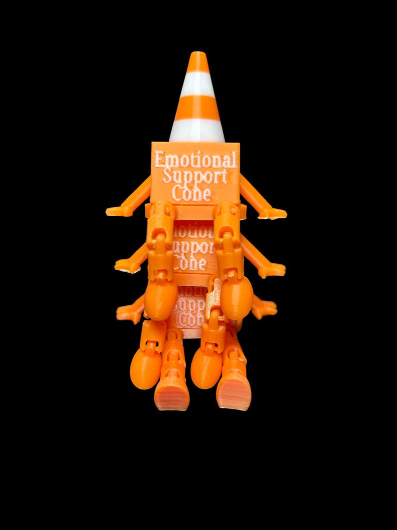 May include: An orange and white traffic cone figure with multiple articulated orange arms and legs. The central block features the text Emotional Support Cone printed in white. The figure has a pointed top and a square base with limbs attached.