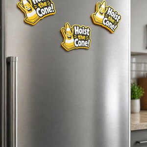 May include: Three yellow and black magnets with the text "Hoist the Cone!" are attached to a stainless steel refrigerator. Each magnet features a smiling traffic cone character.