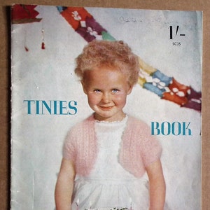 May include: A vintage book cover shows a young girl in a white dress and pink bolero, smiling at the viewer, with a birthday cake in front of her. The cover reads "TINIES BOOK" and "Woollies for 6 months to 3 years by Stitchcraft."