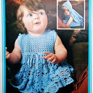 May include: A baby girl wearing a light blue crocheted dress with a matching crocheted bonnet. The dress has a lace trim and a ribbon tie at the waist.