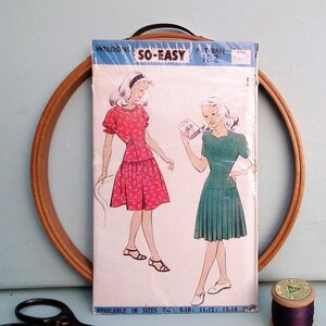 May include: Vintage sewing pattern for a girl's dress. The pattern is called "So-Easy" and is for ages 7 to 14. The pattern shows two girls wearing dresses, one in red with white polka dots and the other in green. The pattern is available in sizes 7-6, 9-10, 11-12, and 13-14.