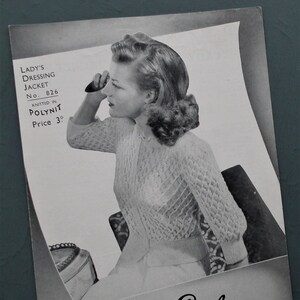 May include: Vintage black and white image of a woman wearing a knitted dressing jacket. The jacket has a delicate openwork pattern. The image is from a "Golden Eagle" pattern, with text that reads "Lady's Dressing Jacket No. 826 Knitted in Polynit".