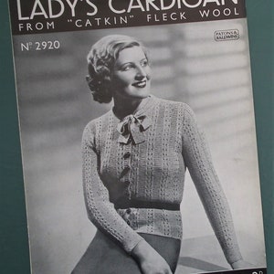 May include: A vintage black and white image of a woman wearing a knitted cardigan. The image is from a knitting pattern, with text that reads "LADY'S CARDIGAN" and "FROM 'CATKIN' FLECK WOOL." The pattern number is 2920.