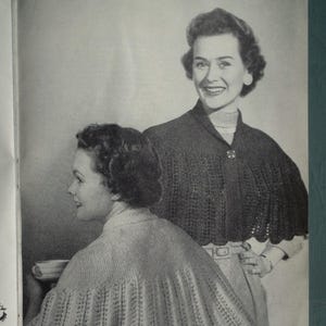Könnte beinhalten: Schwarz-Weiß-Bild von zwei Frauen, die gestrickte Capes tragen. Die Capes haben einen gewellten Rand und werden mit einem Knopf befestigt. Die Frau im Hintergrund lächelt. Das Bild stammt aus einer Vintage-Zeitschrift.