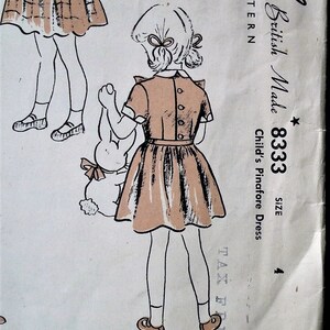 Op de afbeelding: Vintage naaipatroon voor een kinder pinafore jurk. De illustratie toont een meisje in een lichtbruine jurk met een geplooide rok, met een knuffelkonijn. Het patroon is gemarkeerd met "British Made 8333, Maat 4".