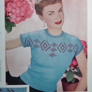 Op de afbeelding: Een vintage mode-tijdschriftfoto toont een vrouw in een lichtblauwe gebreide top. De top heeft korte mouwen en een geometrisch patroon in donkerder blauw en rood. De vrouw lacht, met roze bloemen op de achtergrond. Tekst van pagina 29.