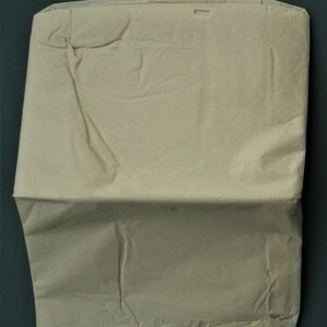 Op de afbeelding: Een gevouwen, beige papieren envelop met een rechthoekige vorm. De envelop heeft een flap aan de bovenkant en een klein rechthoekig gat bij de bovenrand. Het papier heeft zichtbare kreukels en vouwen.
