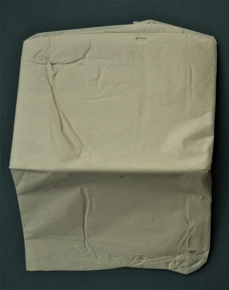 Op de afbeelding: Een gevouwen, beige papieren envelop met een rechthoekige vorm. De envelop heeft een flap aan de bovenkant en een klein rechthoekig gat bij de bovenrand. Het papier heeft zichtbare kreukels en vouwen.