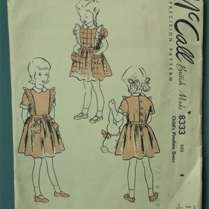 Op de afbeelding: Vintage McCall's naaipatroon voor een kinder pinafore jurk. Het patroon toont illustraties van het jurk ontwerp, gedrukt op verouderd papier. Het jurk ontwerp bevat zakken en een riem. De tekst "McCall" en "Child's Pinafore Dress" zijn zichtbaar.