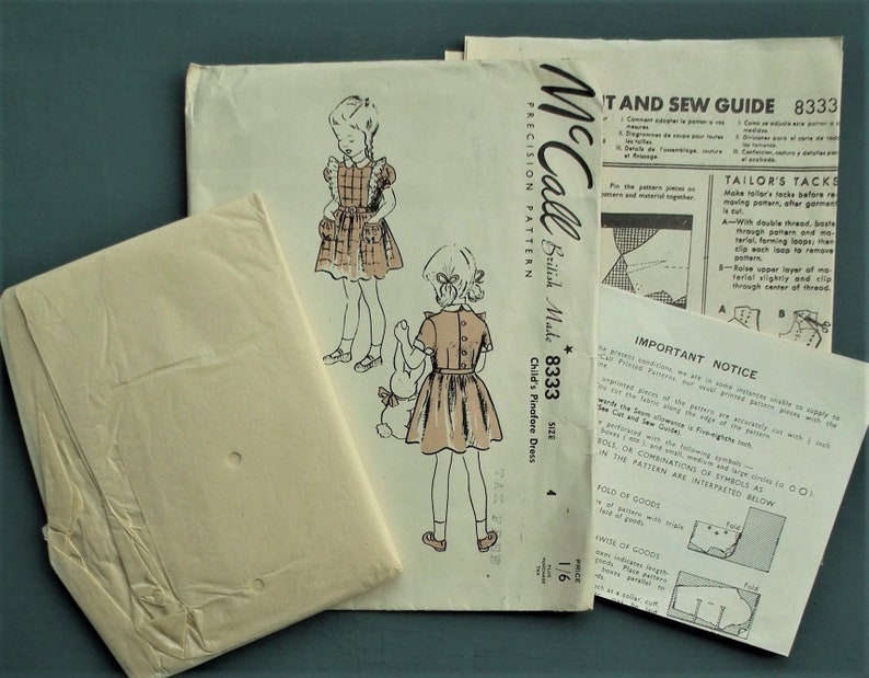 Op de afbeelding: Vintage McCall's naaipatroon voor een kinder pinafore jurk. Het patroonpakket, met het label "British Made", toont illustraties van de jurk en bevat instructies en een knipgids. Maatinformatie is ook zichtbaar.