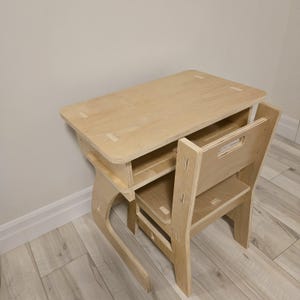 May include: A wooden desk and chair set for children, made of light-colored plywood. The desk has a shelf underneath and the chair has a back and a seat.