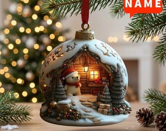 May include: A spherical Christmas bauble featuring a miniature winter scene inside a snow-covered cabin. A small bear wearing a red hat and scarf stands inside the cabin, which is illuminated by a warm light. The ornament hangs from a red ribbon.