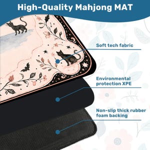 May include: A Mahjong mat featuring a pale pink surface with black cat illustrations, floral vines, and bats. The mat is composed of three layers: a soft tech fabric top, an environmental protection XPE middle layer, and a non-slip thick rubber foam backing.