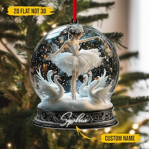 Puede incluir: Adorno de bola de nieve de cristal transparente con una bailarina con tutú blanco y cisnes. El adorno tiene una base negra con el nombre "Sophia" y el texto "CUSTOM NAME". También es visible el texto "2D FLAT NOT 3D".