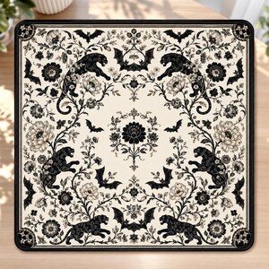 May include: A square desk mat featuring a cream-colored background with a repeating black botanical pattern. The design includes illustrations of black panthers, various blooming flowers, and flying bats arranged in a symmetrical layout.