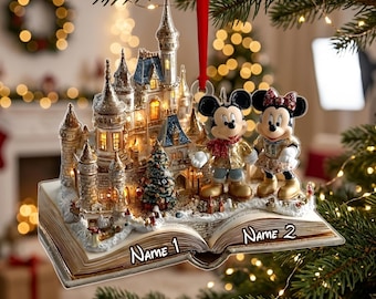 May include: A Christmas tree ornament featuring a detailed castle and two cartoon mice figures standing on an open book. The book pages have the text Name 1 and Name 2 printed on them. The ornament is suspended by a red ribbon and features gold accents.