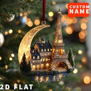 Può includere: Ornamento natalizio con una Torre Eiffel illuminata e una luna crescente. L'ornamento presenta un paesaggio urbano dettagliato e il testo "CUSTOM NAME" e "2D FLAT". È appeso a un nastro rosso.