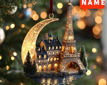 May include: A Christmas ornament featuring a miniature illuminated Eiffel Tower and a crescent moon. The ornament has a detailed cityscape with buildings and trees, and the text "CUSTOM NAME" and "2D FLAT". It hangs from a red ribbon.