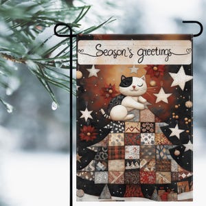 Könnte beinhalten: Eine dekorative Gartenflagge mit einer Katze mit schwarz-weißem Muster, die auf einem Patchwork-Quilt-Design ruht. Die Flagge trägt den Text "Season's greetings" und ist mit Sternen und Blumen verziert. Der Hintergrund ist eine Mischung aus Braun und Schwarz.