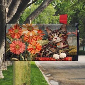 Może przedstawiać: Ozdobna skrzynka pocztowa z motywem kota i pomarańczowymi i białymi kwiatami. Kot ma wzór patchwork z białymi łapami i żółtymi oczami. Skrzynka pocztowa jest zamontowana na drewnianym słupie.