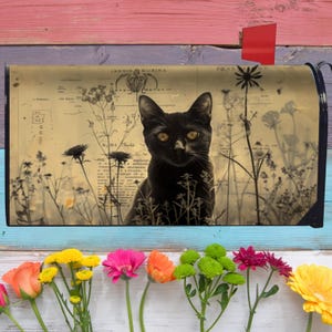 Peut inclure: Un chat noir aux yeux jaunes est représenté sur un couvercle de boîte aux lettres. Le motif comprend une impression botanique vintage avec des fleurs sauvages. La boîte aux lettres a un drapeau rouge et est posée sur un fond en bois coloré avec des fleurs.