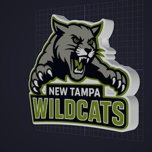 May include: A three-dimensional sign featuring a gray wildcat mascot with green eyes and sharp claws, positioned above the text NEW TAMPA WILDCATS in bold white and green lettering on a black background, with a white border and thick white sides.