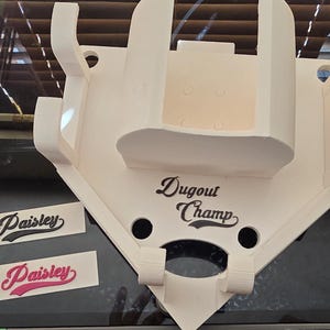 May include: A white baseball-shaped dugout display with the text "Dugout Champ". Two "Paisley" decals are also visible. The display has a unique design with multiple slots and a shelf.