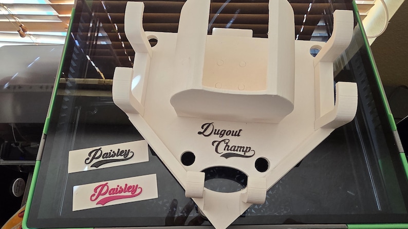 May include: A white baseball-shaped dugout display with the text "Dugout Champ". Two "Paisley" decals are also visible. The display has a unique design with multiple slots and a shelf.