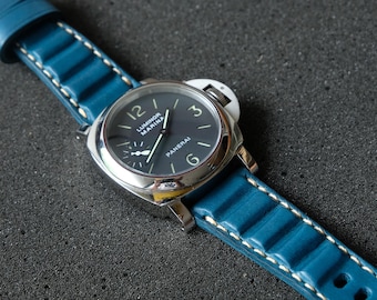 May include: A close-up of a wristwatch with a dark blue face and a silver case. The watch has a blue leather band with white stitching. The watch face displays the brand name "Panerai".