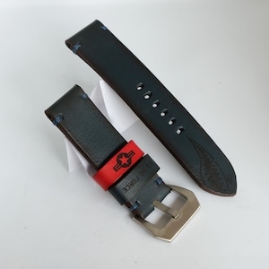 May include: Two-piece watch strap in navy blue leather with blue stitching. A red band with a star emblem and "U.S. AIR FORCE" text is attached. The strap has a silver-colored buckle.