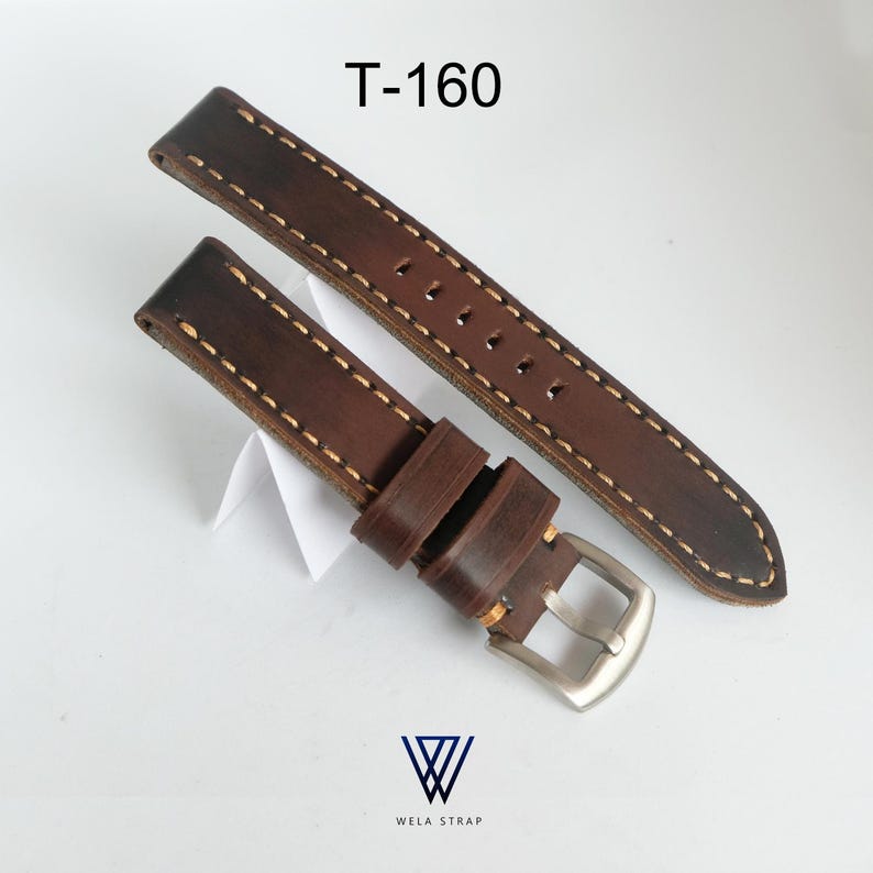 May include: A brown leather watch strap with cream-colored stitching. The strap has a silver-colored buckle and is labeled "T-160". The Wela Strap logo is visible at the bottom.