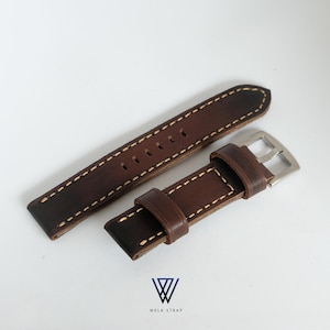 May include: A brown leather watch strap with white stitching and a silver buckle. The strap has a distressed appearance and the text "WELA STRAP" is visible.