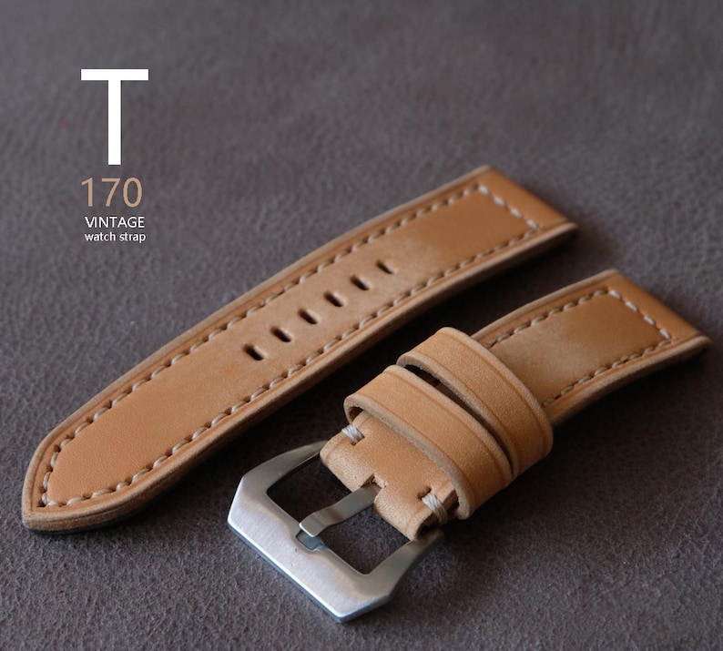 May include: A light brown leather watch strap with white stitching and a silver buckle. The strap has multiple holes for adjustment and the text "T 170 VINTAGE watch strap" is visible.