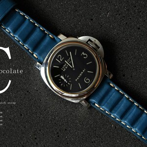 May include: A luxury wristwatch with a black face and silver casing, featuring a blue leather strap with white stitching. The watch face displays the brand name "PANERAI". The image includes the text "Chocolate" and "Letaher watch strap".