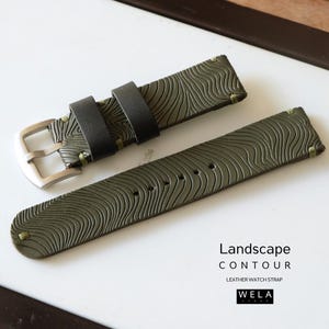 May include: An olive green leather watch strap with a landscape contour design. The strap features black loops, a silver buckle, and green stitching. The text "Landscape Contour Leather Watch Strap" is visible.