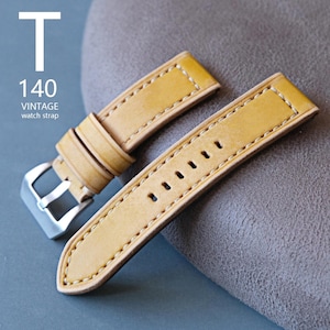 May include: A tan leather watch strap with white stitching and a silver buckle. The strap has the text "T 140 VINTAGE watch strap" in white. The strap is made of a soft, textured leather.