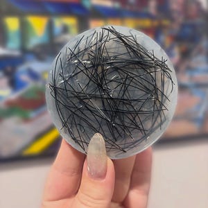 May include: A circular, translucent resin coaster or decorative disc featuring a dense, chaotic arrangement of thin, black hair-like fibers embedded throughout the clear material, creating a stark contrast between the dark strands and the pale base.