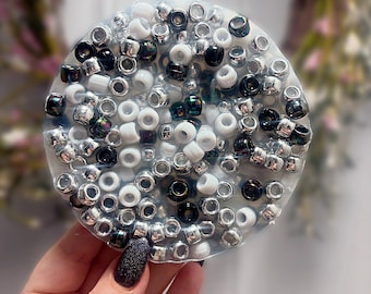 May include: A circular coaster made of clear resin embedded with a dense collection of small beads. The beads are a mix of metallic silver, solid white, and glossy black, creating a textured, multi-dimensional surface across the entire round shape.