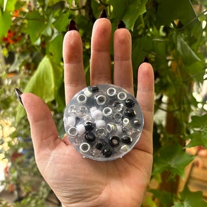 May include: A clear resin tray filled with black, white and silver beads. The tray is being held in a person's hand.
