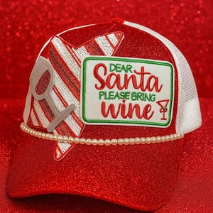 May include: A red and white trucker hat with the text "Dear Santa Please Bring Wine". The hat features a pearl bead trim, a wine glass graphic, and a candy cane design. The hat is perfect for the holiday season.