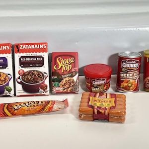 May include: A collection of miniature food items, including Zatarain's Jambalaya and Red Beans & Rice boxes, a Stove Top box, Campbell's Chunky soup cans, Hormel Chili can, a Bomb Burrito, and a package of Wieners.